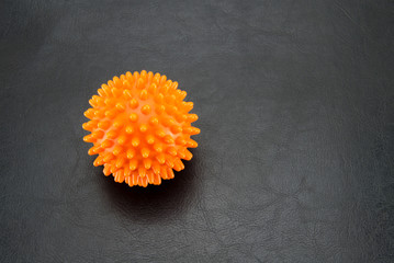 An orange ball with spikes in the form of a virus on a black textured background on the left side of the background. The concept of disease, infection and coronavirus.
