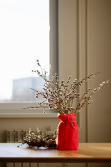 a vase with a bouquet of willow branches with fluffy buds, a homemade wreath of willow branches on a wooden table in the sunlight in brown tones © Elena
