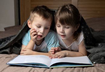 Fototapeta na wymiar boy and girl are reading a book under the coverlet