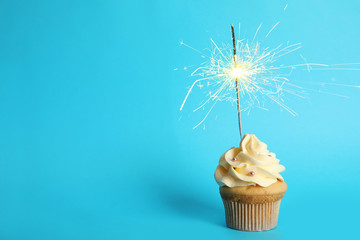 Birthday cupcake with sparkler on light blue background. Space for text