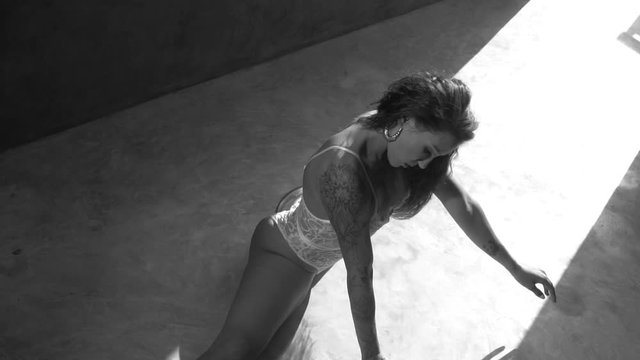Beautiful acrobatic in white lace lingerie dancing in the studio over concrete wall background - black and white video in slow motion