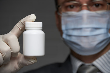 a man with a mask on his face for antivirus individual protection shows a white blank bottle for medicine, pills - healthcare and medicine concept, prevention tips