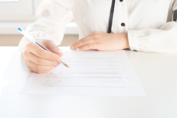 Female hands write with a pen on a sheet of paper, fill out a questionnaire