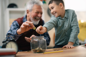 Grandpa and grandson saving money. Grandfather teaching grandchild how to save money.