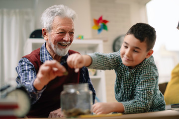 Grandpa and grandson saving money. Grandfather teaching grandchild how to save money.