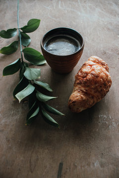 Cappuccino coffee and croissant on wooden background on the table. Perfect breakfast in the morning. Rustic candid style.