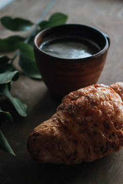 Cappuccino coffee and croissant on wooden background on the table. Perfect breakfast in the morning. Rustic candid style.