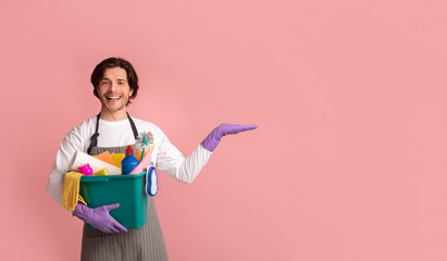 Cheerful Young Man Holding Basket With Cleaning Supplies And Pointing Aside