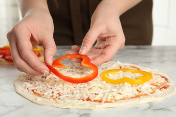 Obraz na płótnie Canvas Woman adding bell pepper to pizza white marble table, closeup