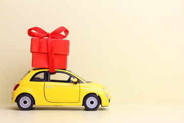 a toy yellow car  with  a red box  on the roof.  Present  delivery concept. 