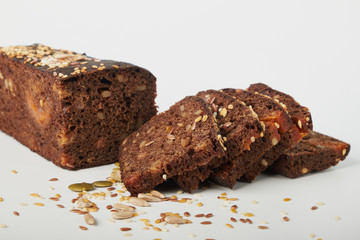 fresh bread with various seeds (pumpkin, dried apricots, flax, sunflower, sesame, prunes) is decorated with wheat ears isolated on a white background.