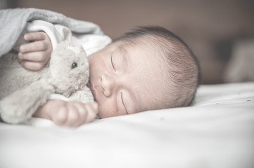 Newborn baby sleeping on bed with little rabbit.Family and love concept.Asian kid.