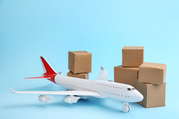 Airplane model and carton boxes on light blue background. Courier service