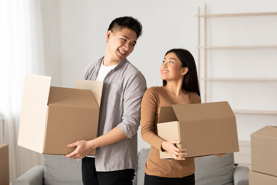 Happy asian family holding cardboard boxes in new flat