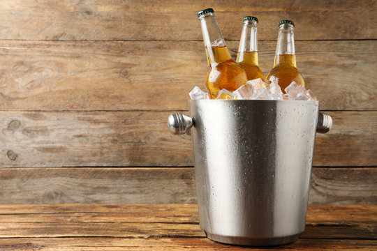 Metal bucket with beer and ice cubes on wooden background. Space for text