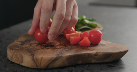 closeup man cutting cherry tomatoes on olive board