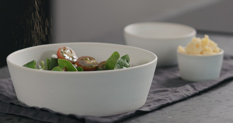 man seasoning salad with kumato tomatoes and spinach in white bowl