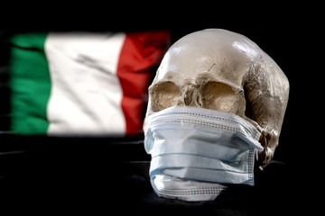 A human skull in a medical mask on the background of the Italian flag . Concept: mortality in Italy from coronavirus, global pandemic, infection with a deadly virus.