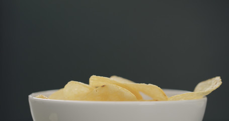 potato chips in white bowl on black background closeup