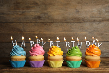 Birthday cupcakes with burning candles on table against wooden background. Space for text