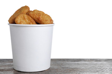 Bucket with tasty chicken nuggets on wooden table against white background. Space for text