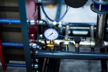 pressure gauge psi meter in pipe and valves of water system industrial focus left closeup white light defocus blur background