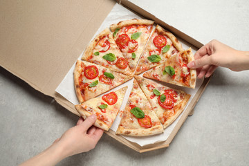 People taking slices of delicious pizza Margherita from box at light grey table, top view