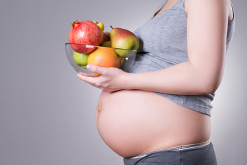 Pregnancy and nutrition - pregnant woman with fresh fruit on gray background