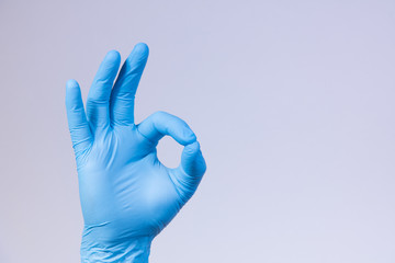 Ok sign is showed by right man hand in a blue medical glove on a white background. Okay. All right