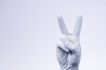 V sign is showed by right man hand in a white medical glove on a white background. The symbol of Victory. Victory over a virus.
