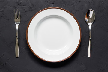 Empty plate with spoon and fork on black table
