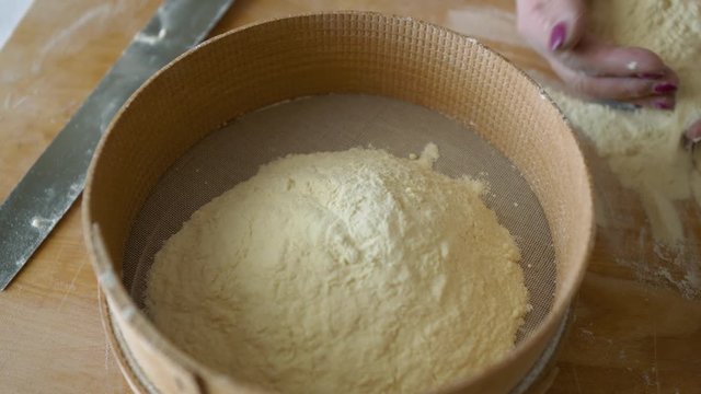 Close Up view of female hand pouring semolina flour into wooden sieve