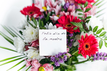 white card for a bouquet with the inscription Happy Mother's Day in spanish in a bright beautiful bouquet of flowers