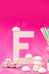 Letter E with marshmallow decorations with straws on a pink background