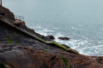 Wet and mossy stone stairs that descend between the rocks to the sea in Donostia, San Sebastian,...