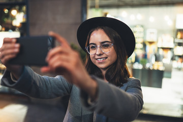 Smile girl take selfie outdoors using mobile smartphone on background bokeh light in night city, womn hold in hands sellphone, online wi-fi internet