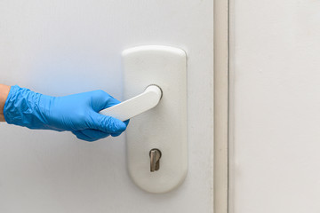 Naklejka premium A female hand in a blue protective glove holds a doorknob and is about to open the door. Antibacterial prophylaxis in times of viruses and infections. Health and protection concept. Horizontal view.