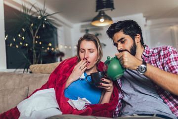 Handsome man taking care of his sick girlfriend lying on the sofa