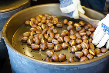 male hands stirring and roasting delicious organic chestnuts on a gas barrel stove with wooden ladle
