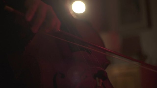 Close up shot of female cello player hands playing cello in concert room with red lightning. Cello bow.