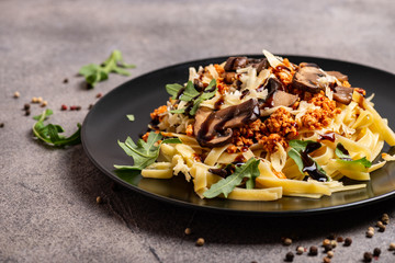 Bolognese pasta with mushrooms and arugula poured balsamic sauce. Close-up.