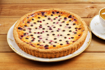 Homemade berry pie with chocolate drops and cup of coffee cappuccino on wooden table. Angle view.