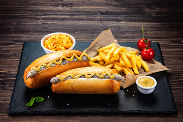 Hot dogs, French fries and vegetables on black stone board