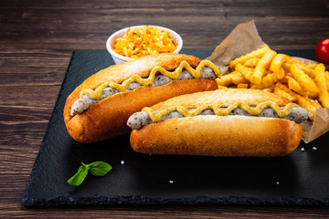 Hot dogs, French fries and vegetables on black stone board