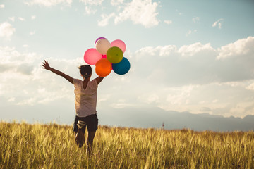 Cheering young asian woman on grassland with colored balloons