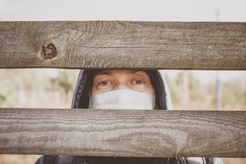 Woman in a disposable medical mask near a wooden fence. Coronavirus epidemic.  Covid 19. Pandemic.