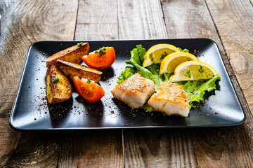 Fish dish - fried cod fillet with vegetables on wooden table