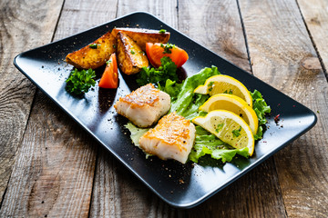 Fish dish - fried cod fillet with vegetables on wooden table