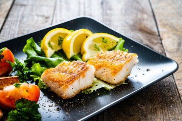 Fish dish - fried cod fillet with vegetables on wooden table