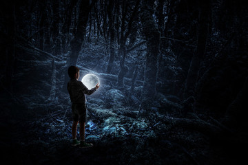 Boy holding moon at night in the forrest
